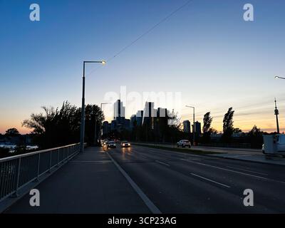 Wien, Österreich - 22. Oktober 2024: Abenddämmerung über einer modernen Skyline von einer Brücke mit Autos, Bäumen und Lichtern in Wien, Österreich. Stockfoto