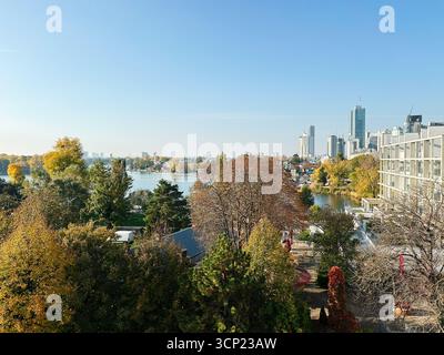 Wien, Österreich - 22. Oktober 2024: Lebhafte Herbstszene einer Stadt am See mit bunten Bäumen und modernen Hochhäusern in Wien, Österreich. Stockfoto