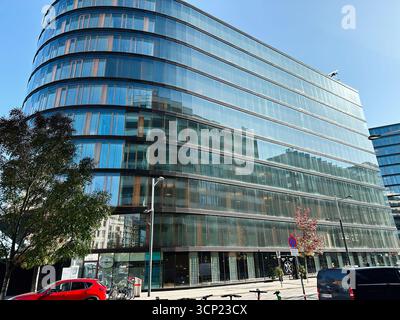 Wien, Österreich - 22. Oktober 2024: Die elegante Glasfassade reflektiert den blauen Himmel entlang eines modernen geschwungenen Bürogebäudes erste Campus neben einer geschäftigen Stadtstraße Stockfoto