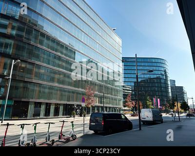 Wien, Österreich - 22. Oktober 2024: Eine sonnige Stadtstraße mit verglasten Bürogebäuden, Fahrrädern, Lieferwagen und Fußgängern in einem modernen Geschäftsviertel in Vie Stockfoto