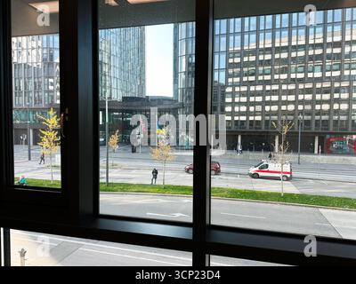 Wien, Österreich - 22. Oktober 2024: Urbane Szene aus Glas die Ikone Wolkenkratzer, Fahnen, Fußgänger und ein weißer Krankenwagen auf einer Stadtstraße in Wien, Au Stockfoto