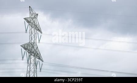 Nahaufnahme eines Hochspannungsnetzturms mit mehreren Kabeln auf bewölktem Himmel. Das Bild zeigt die Energieinfrastruktur, die Elektrizität Stockfoto