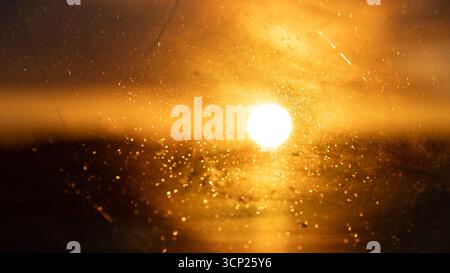 Goldener Sonnenuntergang durch Glas mit Wassertropfen und Reflexen. Die glühende Sonne erzeugt einen warmen abstrakten Hintergrund, perfekt zur Illustration von t Stockfoto