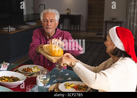 Senior Pärchen schneiden und geben an Bord an einem Feiertagstisch Brot mit geröstetem Gemüse und Wein Stockfoto