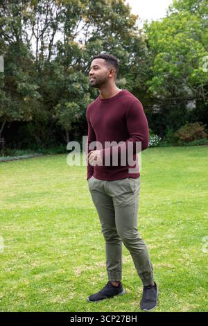 afroamerikaner, der auf dem Garten steht, trägt einen kastanienbraunen Pullover und grüne Hosen Stockfoto