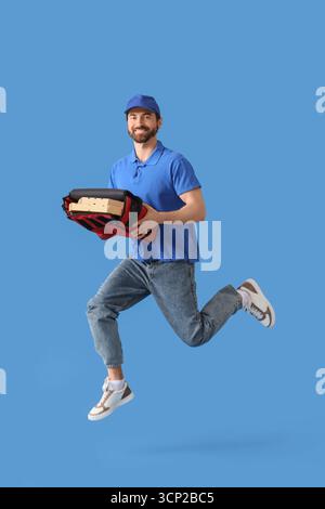 Männlicher Kurier mit Pizzakästen in Lebensmittelbeutel, der auf blauem Hintergrund springt Stockfoto