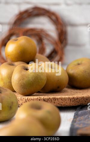 Eine vertikale Nahaufnahme zeigt eine gemütliche Herbstszene mit einem Stapel rustikaler grüner und gelber Äpfel auf einem runden Korkuntersetzer. Der Softfokus im Vordergrund Stockfoto