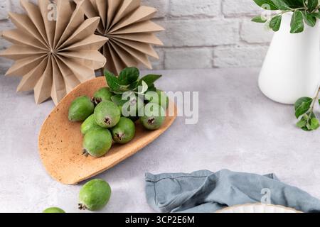 Ein flaches, minimalistisches Stillleben mit frischen, ganzen Feijoa-Früchten auf einer einzigartigen, modernen Terrakottafarbenen Platte. Die Früchte sind gegen eine sim angeordnet Stockfoto