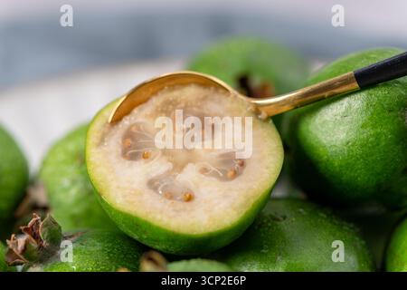 Eine Nahaufnahme einer halbgeschnittenen Feijoa-Frucht aus der Nähe, die ihr helles, goldfarbenes Fruchtfleisch und ihr einzigartiges Sternmuster offenbart. Ein kleines Gold Stockfoto