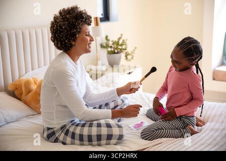 Verschiedene Mutter und Tochter spielen Make-up mit Pinsel, Palette auf dem Bett mit Teddybär Stockfoto