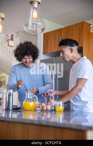 Abwechslungsreiches Vater und Sohn kochen Frühstück auf Marmor Kücheninsel mit Brot und Orangensaft Stockfoto