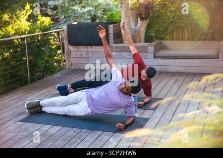 Afroamerikanische Männer, die Seitenplanken auf dem Hinterhof mit Yogamatten und Wasserflasche spielen Stockfoto