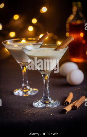 Zwei Gläser Egg Nog mit Rum und Eiern und Zimtstangen und Bokeh-Lichtern im Hintergrund Stockfoto