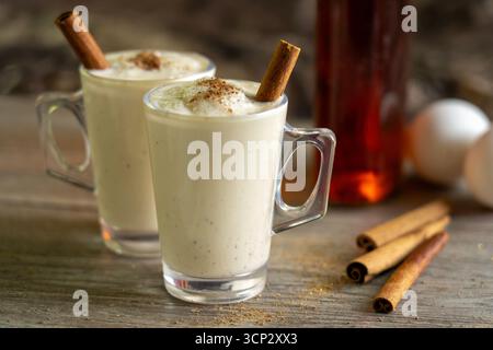 Zwei Gläser Egg Nog mit Rum, Muskatnuss, Zimtstangen und Eiern im Hintergrund Stockfoto