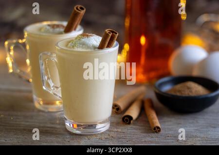 Zwei Gläser Egg Nog mit Rum, Muskatnuss, Zimtstangen und Eiern im Hintergrund Stockfoto