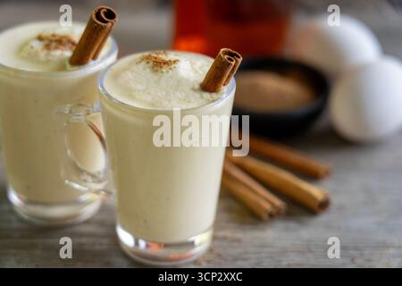 Zwei Gläser Egg Nog mit Rum, Muskatnuss, Zimtstangen und Eiern im Hintergrund Stockfoto