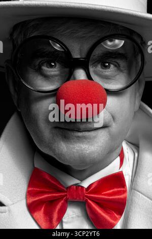 Nahaufnahme selektives Farbporträt eines Clown. Ein älterer Mann mit weißem Mantel und Hut. Stockfoto