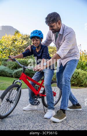 Asiatischer Vater und Sohn, die auf dem Schotterweg mit blauem Helm auf rotem Fahrrad fahren Stockfoto