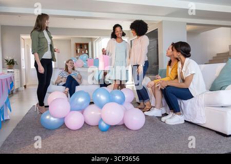 Verschiedene Freundinnen treffen sich im Wohnzimmer und teilen Pastellballons Geschenktüte, verpackte Geschenke Stockfoto