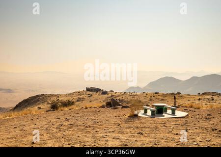 Ein Picknick-Ort überblickt die weite Namib-Wüste vom Spreetshoogte Pass aus mit trüben Ebenen, zerklüfteten Bergen und einem einsamen Haus auf dem Kamm unter dem bri Stockfoto