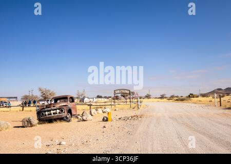 Auf dem Autofriedhof von Solitaire in Namibia befinden sich rostige Oldtimer in der Nähe kleiner Wüstengebäude, die vor Dünen und Bergen liegen und den Charme der Wüste einfangen Stockfoto