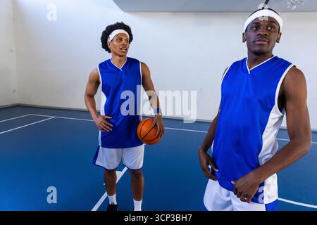 afroamerikanische Mannschaftskameraden in blauen Trikots stehen auf dem Platz und halten Basketball am Basketball Stockfoto