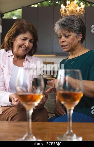 Verschiedene Freundinnen, die sich zu Hause nahe auf das Sofa lehnen und ein Smartphone mit Rosébrille ansehen Stockfoto