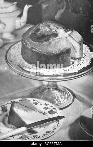 Aus einem vulkanischen Ofen: Ein großer Biskuitkuchen auf einem Glaskuchenständer und ein Stück auf einem Beistellteller. Aus einem gedruckten Foto, das ursprünglich in der Publikation erschien, The Vulcan Cook Book, das 1936 von der Vulcan Stove Company in Exeter, England, veröffentlicht wurde. Stockfoto
