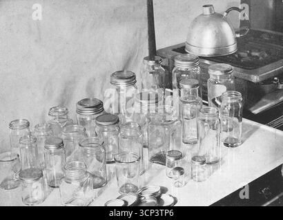 Eine große Ausstellung von Glasgläsern aus den 1930er Jahren, die für die Herstellung von Papierkonfitüren verwendet werden, auf einer emaillierten Arbeitsplatte. Aus einem gedruckten Foto, das ursprünglich in der Publikation erschien, The Vulcan Cook Book, das 1936 von der Vulcan Stove Company in Exeter, England, veröffentlicht wurde. Stockfoto
