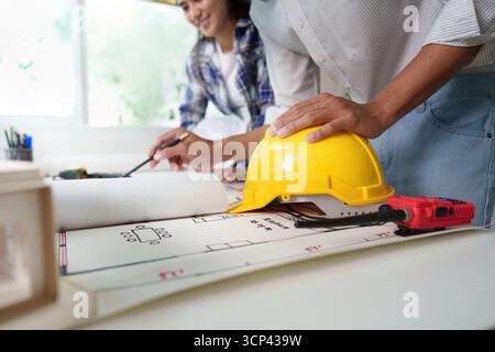 Ingenieurplanung. Junger Ingenieur, der an Bauplänen arbeitet, mit einem Bauhelm auf dem Tisch. Stockfoto