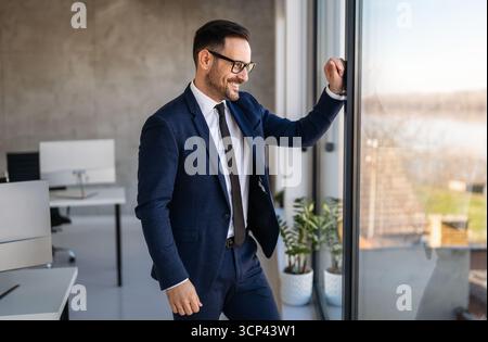 Porträt eines lächelnden Geschäftsmannes, der im Büro steht. Genießen Sie einen erfolgreichen Tag Stockfoto
