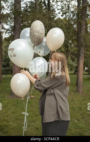 Schwangere Frau, die im Park Babyschauballons hält Stockfoto