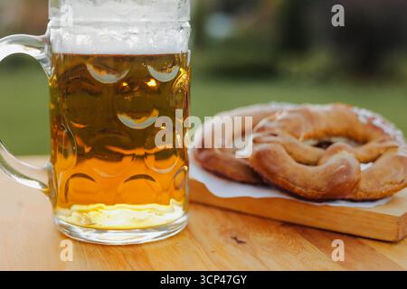 Ein Glas Lagerbier mit Schaum und frisch bayerischen Brezeln auf einem Holztisch. Oktoberfest-Menü. Stockfoto