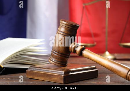 Hammer, Buch und Waage auf Holztisch vor der Flagge Frankreichs, Nahaufnahme Stockfoto