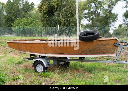Ein altes, rostiges Boot sitzt ruhig auf einem Anhänger, umgeben von üppigem Grün und dickem, bewachsenem Gras Stockfoto