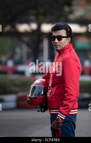 Ein lächelnder Mann gibt ein Siegeszeichen und posiert mit einem roten Motorradhelm Stockfoto