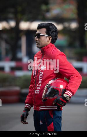 Ein lächelnder Mann gibt ein Siegeszeichen und posiert mit einem roten Motorradhelm Stockfoto