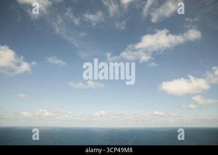 Blauer Himmel mit surrealen Wolken, die über dem Meer verstreut sind Stockfoto