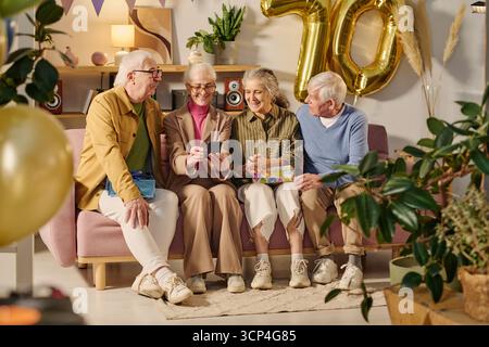 Eine Gruppe älterer Freunde sitzt auf dem Sofa lachend und schaut auf das Smartphone Stockfoto