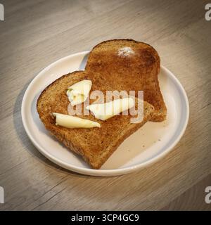 Warme gebutterte Scheiben Toast/geröstetes Brot auf einer weißen Platte, die in Butter getaucht ist und langsam schmilzt Stockfoto