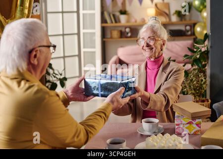 Seniorin erhält während der Feier ein Geschenk vom Seniorenmann Stockfoto