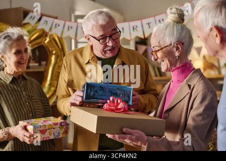 Seniorenmann schenkt Seniorenfrau lächelnd ein Geburtstagsgeschenk Stockfoto