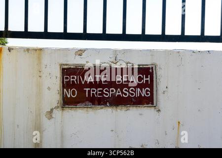 Schild mit der Aufschrift "Private Beach - No Trespassing" an einer Betonmauer unter einem schmiedeeisernen Zaun. Private Strände, Konzept mit eingeschränktem Zugang Stockfoto