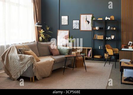 Modernes Wohnzimmer mit modernen Möbeln, dekorativen Pflanzen, gerahmten Kunstwerken an der Wand, offenen Regalen mit Büchern und Accessoires, gemütlichem Sofa mit Kissen, Couchtisch, Arbeitsbereich Stockfoto