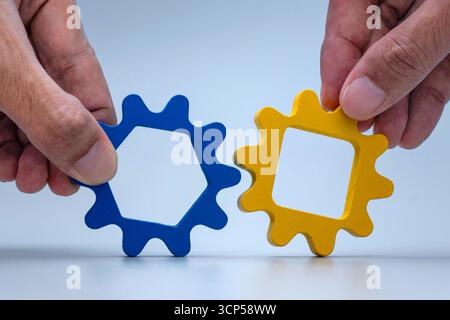 Hände halten blaues Zahnrad und gelbes Zahnrad zusammen, um zu verriegeln. Teamarbeit, Zusammenarbeit, Zusammenarbeit, Partnerschaft, Führung, und Zusammenarbeit Stockfoto