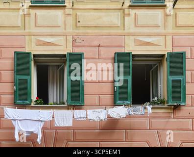 Wäscherei hängt zum Trocknen vor den Fenstern eines alten Gebäudes, mit der gelben und orangen Fassade im Trompe l'oeil Stil, Genua, Italien Stockfoto