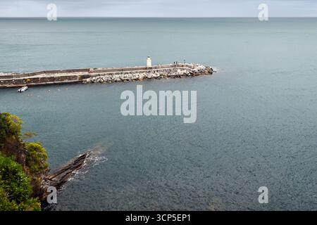 Erhöhter Blick auf den Leuchtturm auf dem Mole, der sich in den Golfo Paradiso erstreckt, an einem bewölkten Frühlingstag, Camogli (Genua), Ligurien, Italien Stockfoto