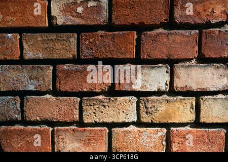 Nahaufnahme einer alten Ziegelwand mit verwitterter Textur, die natürliche Farben und raue Oberflächendetails zeigt. Stockfoto