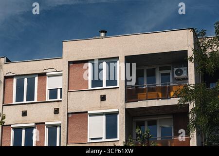 Nahaufnahme der obersten Stockwerke eines alten vorgefertigten Apartmentgebäudes mit sichtbaren Rissen, Klimaanlage und Balkonen unter einem klaren blau Stockfoto