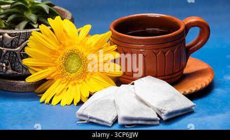 Aromatisches Stillleben mit einer Tasse Tee aus Steingut, einer gelben Gerbera Gänseblümchen und Teebeuteln Stockfoto